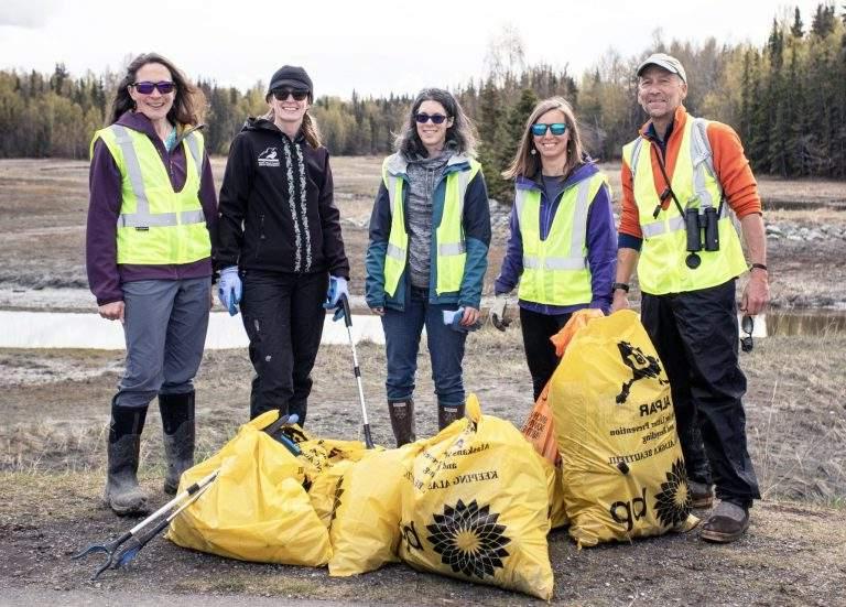 Volunteers post with their grabbers and yellow bags full of trash at an estuary surrounded by trees.